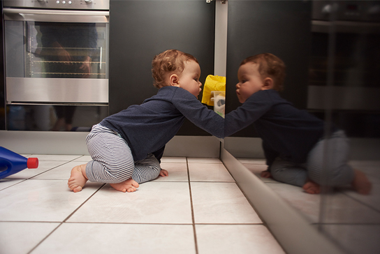 A toddler exploring the contents of a kitchen cabinet.