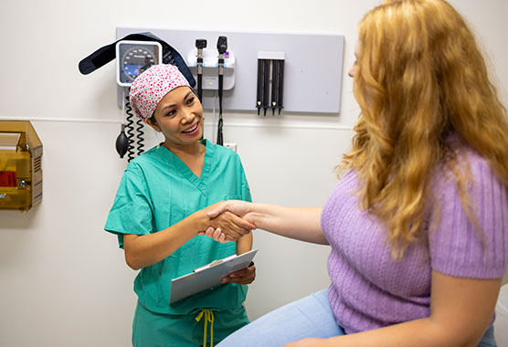Female patient shaking hands with a provider in scrubs in an exam room