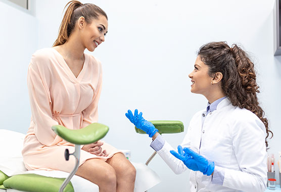 Woman sitting on exam table smiling while talking to her female health care provider