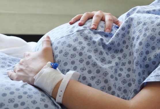 Pregnant woman lying in a hospital bed with her hands on her stomach