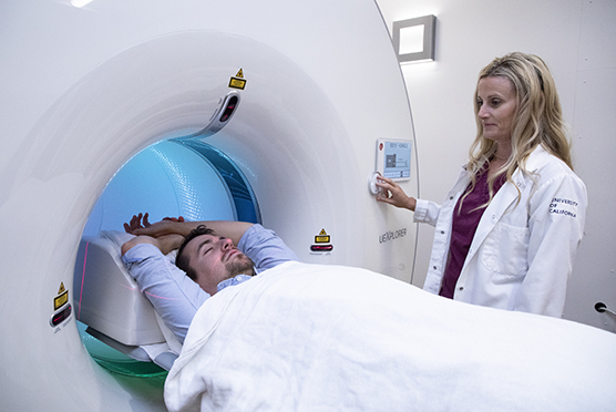 Male patient going into a medical imaging machine and a female provider in a white coat starting the scan 