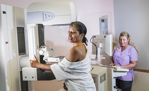 An African-American woman in her 40s wearing a hospital gown,  getting a mammogram.