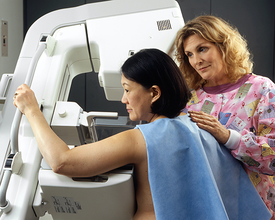 A female technician positioning a woman at an imaging machine to receive a mammogram