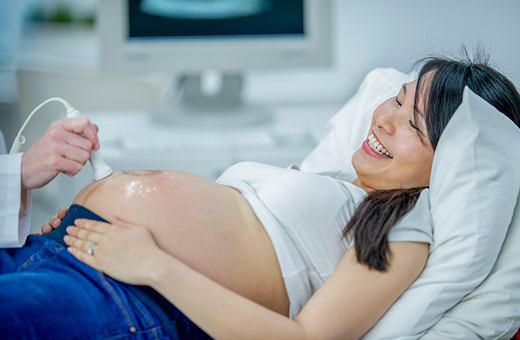 Smiling pregnant woman getting an ultrasound on her stomach.
