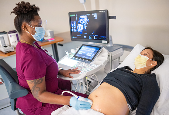 Ultrasound technician using an ultrasound wand on pregnant woman’s belly while she’s laying down.