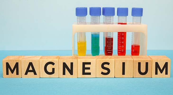 Wooden blocks spell out the word “magnesium” with colorful plastic test tubes in the background.