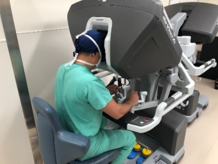 man in green scrubs sitting at robotic surgery instrument looking through video lens