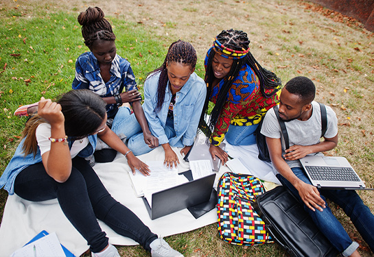 Group of five Black college students studying on the lawn