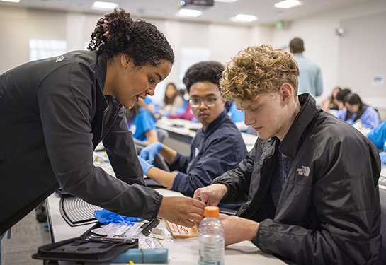 Elise Fannon, general surgery research resident at UC Davis Health, shows AvenueM students some tricks for suturing. 