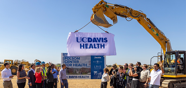 A construction worker uses a large crane to lift up a sign that says “UC Davis Health” to unveil a large sign 
