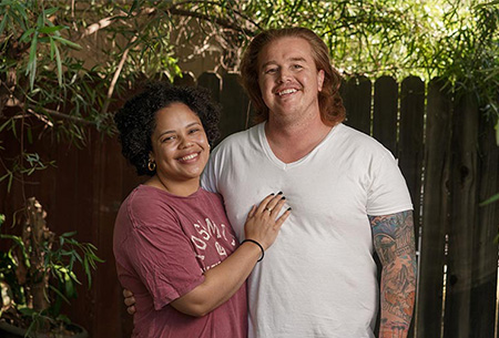 Woman with short black hair and pink T-shirt puts arms around man with red hair and white T-shirt