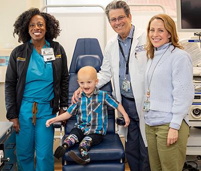 A child sitting in a chair in a doctor’s office posing for a photo with three adults. 