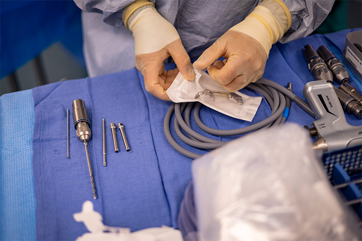 A person wearing surgical gloves opens the MISHA implant, wrapped in a sterile plastic bag on a table of surgical tools.