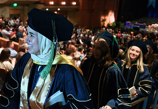A medical student in blue graduation robe walks up a stairway in an auditorium 