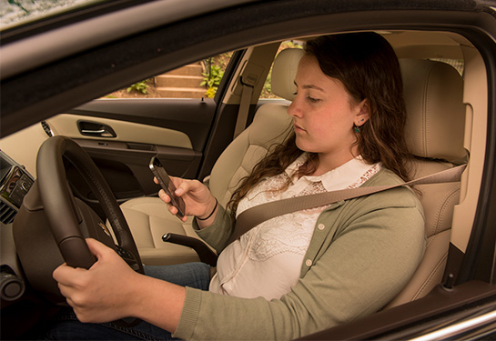 Teenager behind the wheel of parked car looking at cellphone  