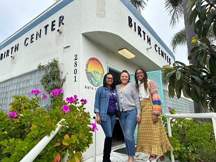 Three representatives of the California Black Women's Health Project stand together for a photo in front of a birth center.
