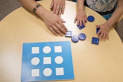 Doctor and pediatric patient test fitting geometric shapes in to their cut-out puzzle.  