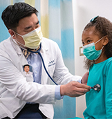 UC Davis pediatrician Christopher Kim provides care during an annual exam while wearing a photo button to help ease patient’s fears of providers in COVID-19 personal protective gear.