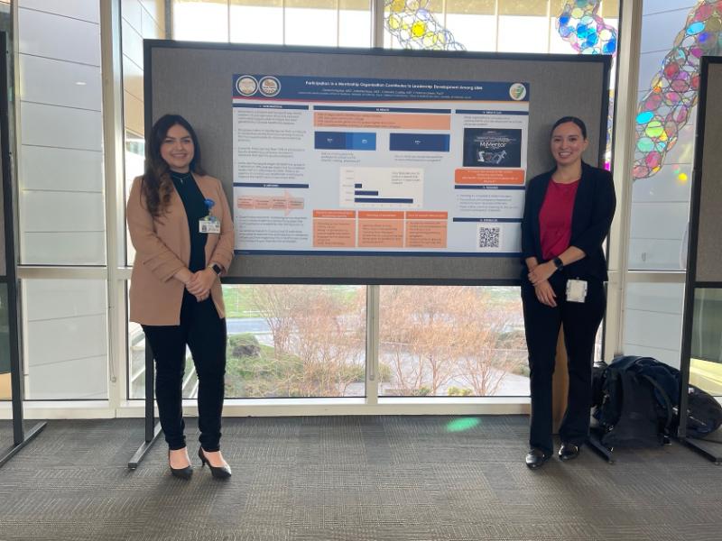 Two students standing in front of a research poster about mentorship for pre-med students