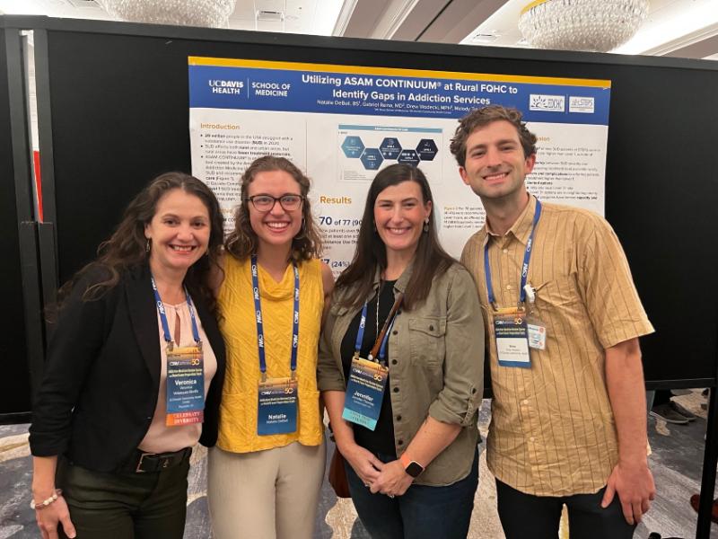Four people standing in front of a research poster at a conference 