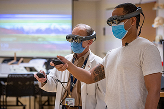 Michael Edwards and neurology resident Edwin Kulubya use mixed reality goggles.
