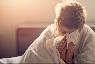A child in bed, sneezing into a tissue.