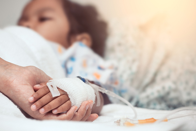 An adult holding a child's hand in a hospital bed.