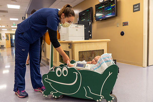 Nurse transporting infant patient using portable bed and wireless monitor