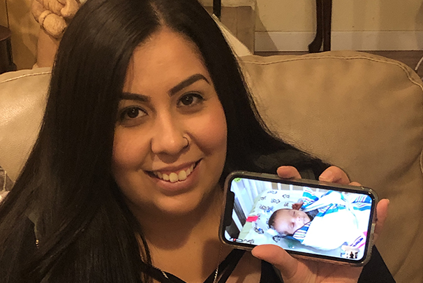 Mom holding phone which is playing video feed of her infant child on NICU webcam
