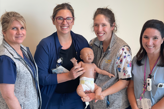 Four women from the uc davis children's hospital team hold a high-tech baby manikin