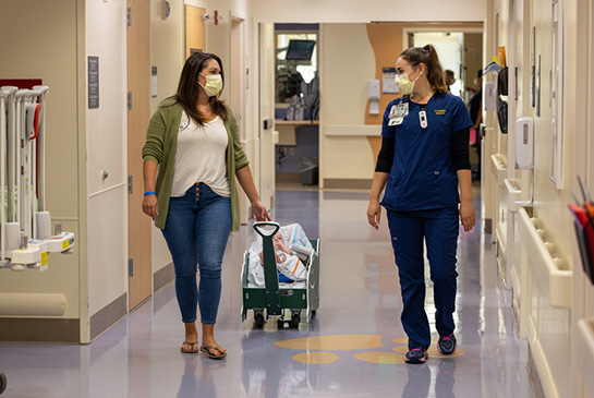 Mother, infant patient, and nurse walking down PICU hallway