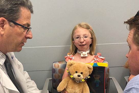 Young girl craniofacial patient holding a teddy bear with doctors