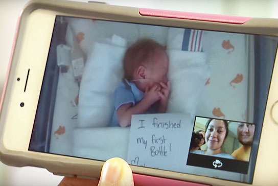 parents watching baby on phone through NICU webcam