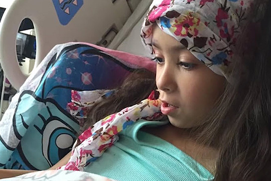 Gianna Saari lying in a hospital bed wearing a scarf.  