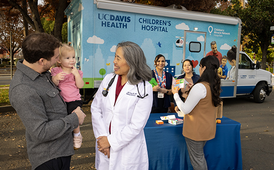 Doctor talking to a father and daughter with the pediatric mobile clinic in the background