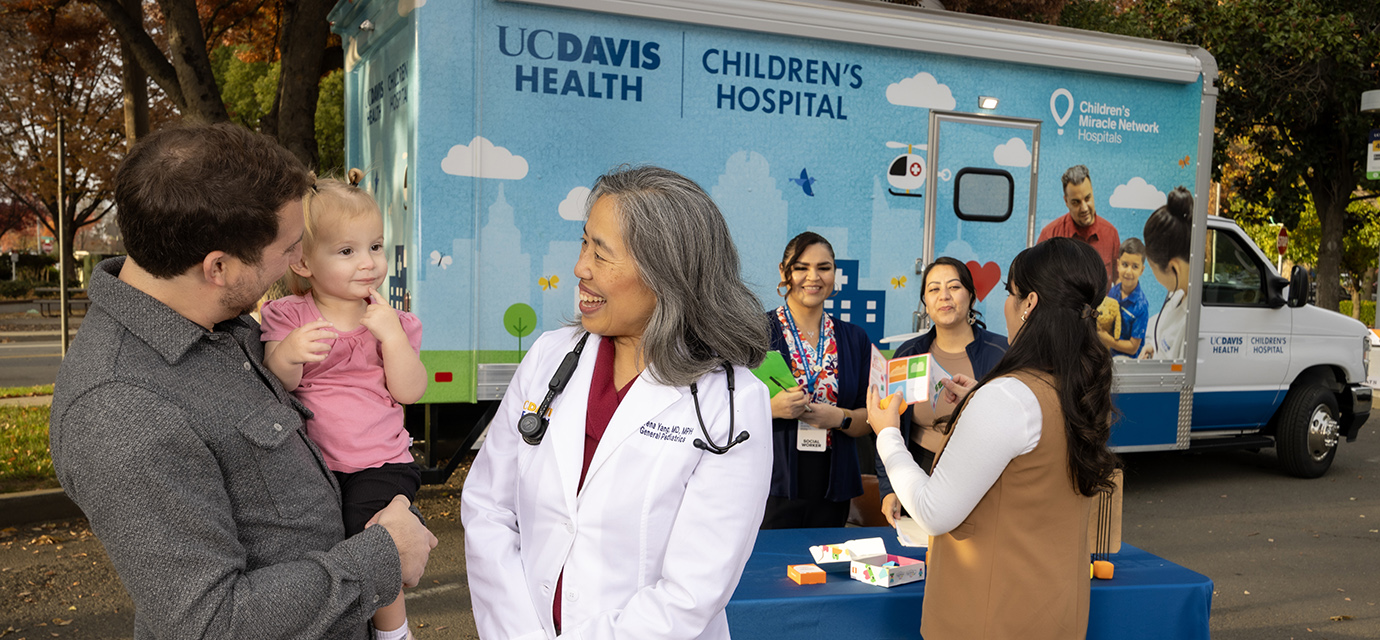 Doctor talking to a dad with his daughter with the pediatric mobile clinic in the background