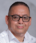 A person wearing glasses and a white shirt, against a grey background.