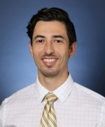 Smiling person in a white dress shirt with a yellow patterned tie.