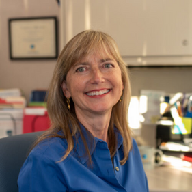 Dominique Ritley smiles in an office wearing a blue shirt.