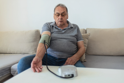 A person is sitting on a couch and measuring their blood pressure with a home blood pressure monitor.
