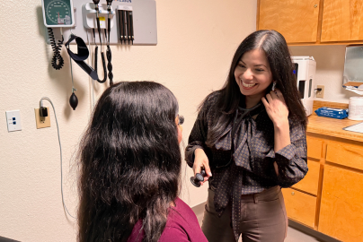 A female doctor wearing jeans and back shirt talks with a patient in a clinic exam room.