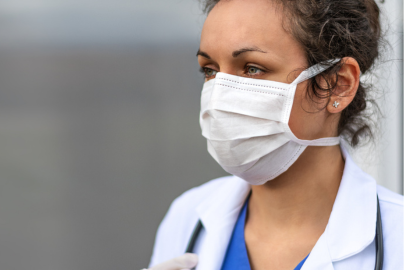 A woman doctor with curly hair looks to the right while wearing a mask.