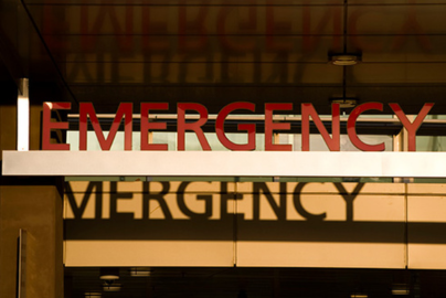 A sign in front of a hospital window reads "Emergency" as its letters reflect off the window.