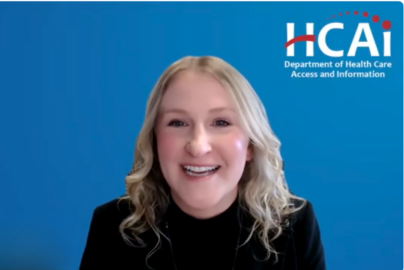 A woman with blonde hair and a dark shirt speaks in front of a background with an HCAI logo.