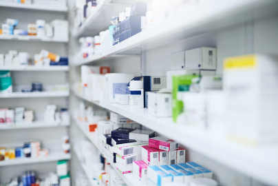 Shelves stocked with various medications and pharmaceutical products in a brightly lit pharmacy.