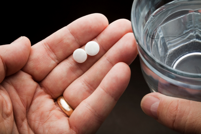 hand with a pill, next to a glass of water.