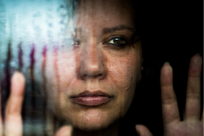 A woman with dark hair looks sad through a rainy window. 