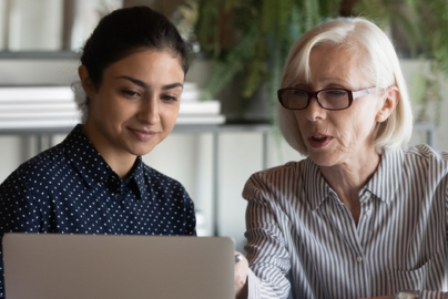 Two women, one older and another younger, sit together looking at a computer.