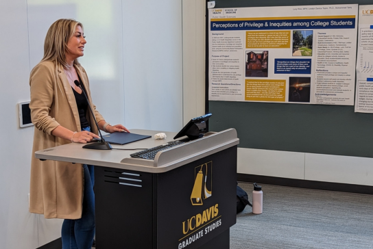 Woman in a long light colored coat speaks behind a podium.