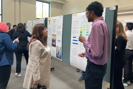 UC Davis Vice Dean for Research Kim Barrett speaks to a male student in a dress shirt about his research poster. 